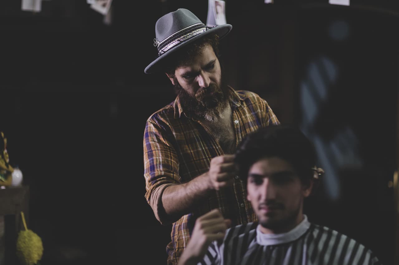 A barber in a hat cutting a young man's hair in a low-lit shop